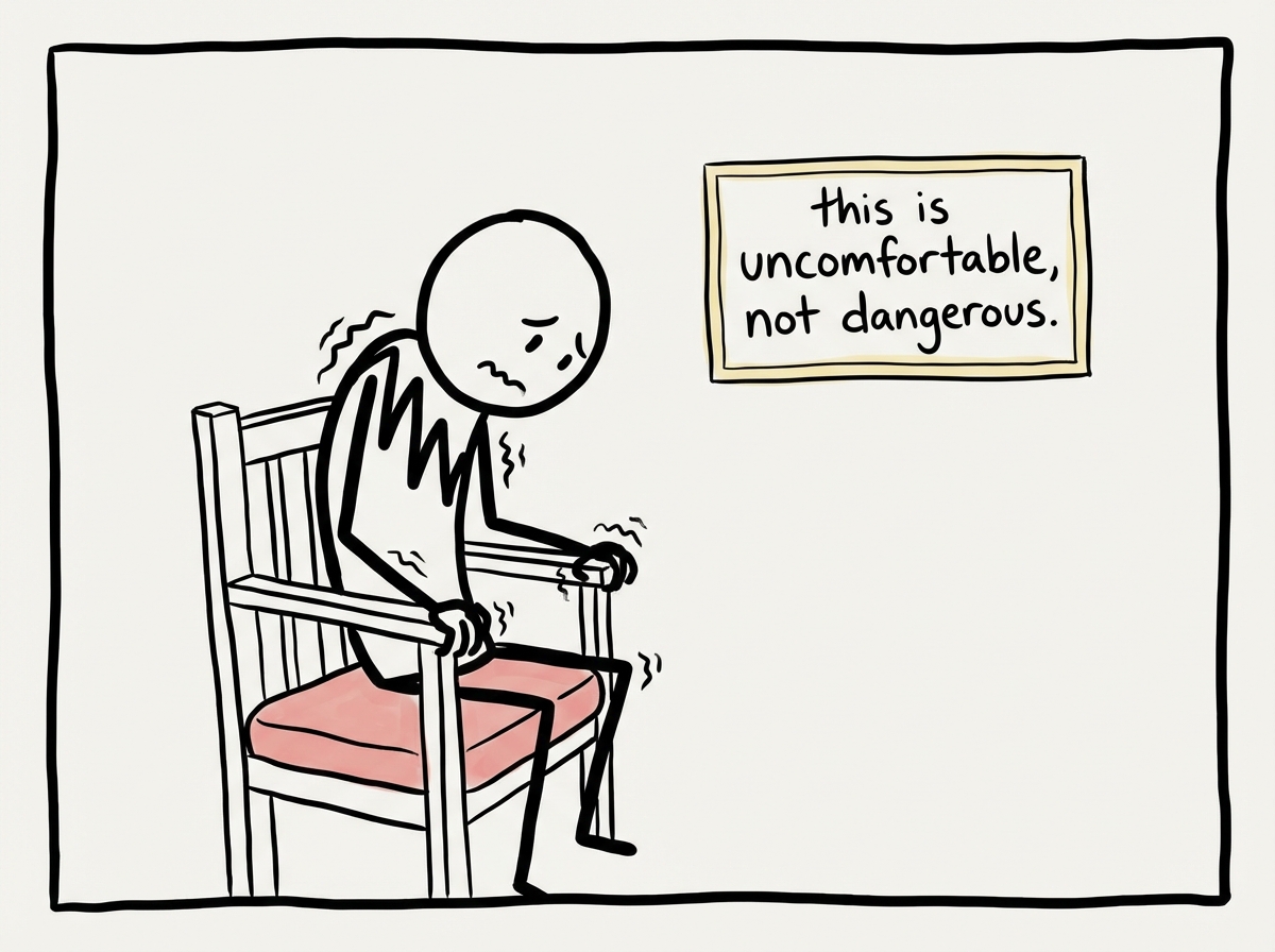 A stick figure sitting with visible discomfort -- hunched shoulders, hands gripping the chair -- while a small sign on the wall reads 'this is uncomfortable, not dangerous'